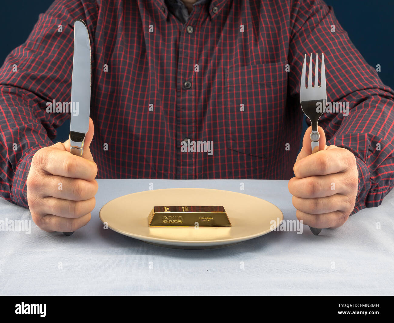 Geschäftsmann sitzt hinter einem Tisch mit Gabel und Messer essfertig Goldbarren serviert auf Teller - Business-Konzept Stockfoto