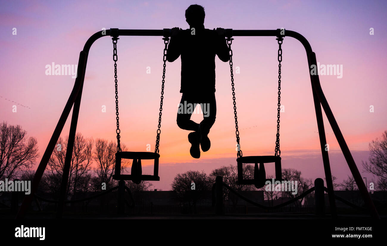 Mann tut Pull Ups auf Schwenkrahmen bei Sonnenaufgang im öffentlichen Park in England. UK Stockfoto