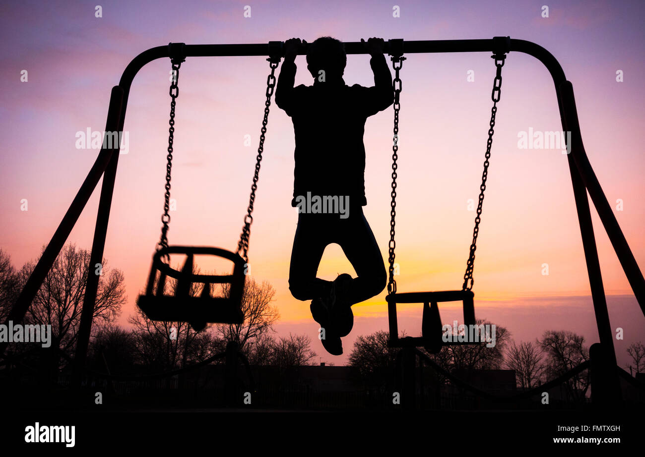 Mann tut Pull Ups auf Schwenkrahmen bei Sonnenaufgang im öffentlichen Park in England. UK Stockfoto