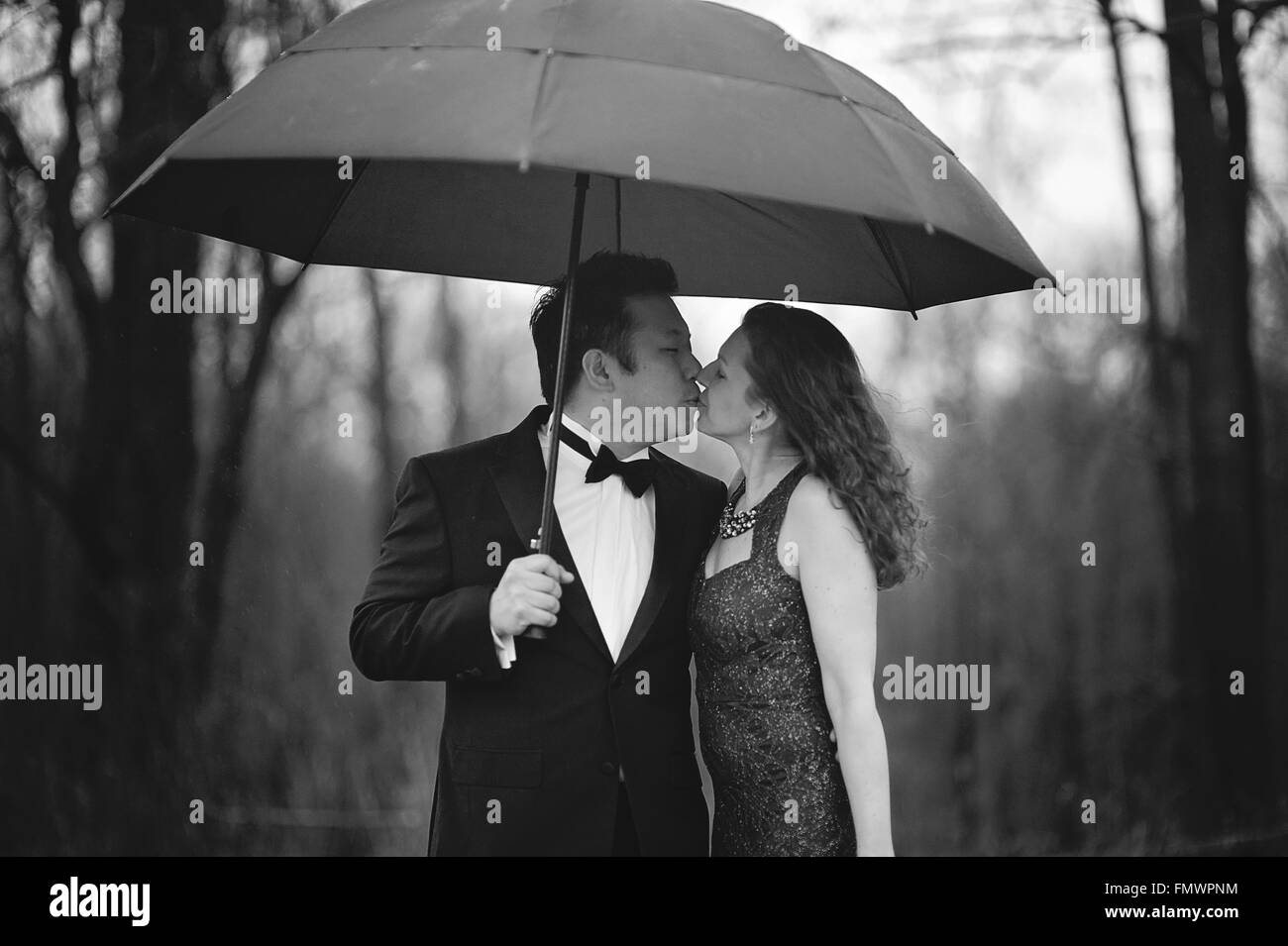 Formale Kuss unter einem schwarzen Regenschirm. Stockfoto