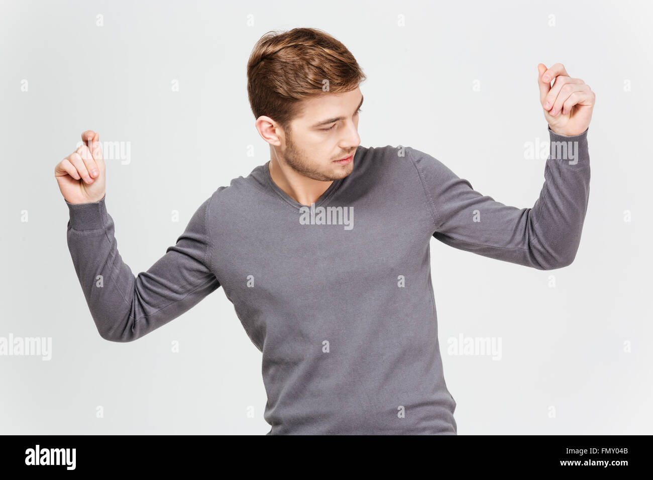 Hübscher zuversichtlicher junger Mann im grauen Pullover mit tanzen hob die Hände auf weißem Hintergrund Stockfoto