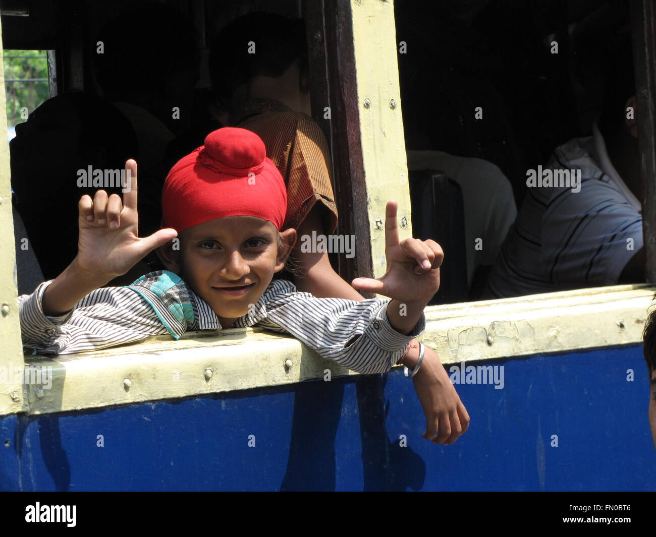 Indischer Junge mit roten Turban Reiten Kangra-Tal-Schnellzug in Indien sieht aus Fenster Stockfoto