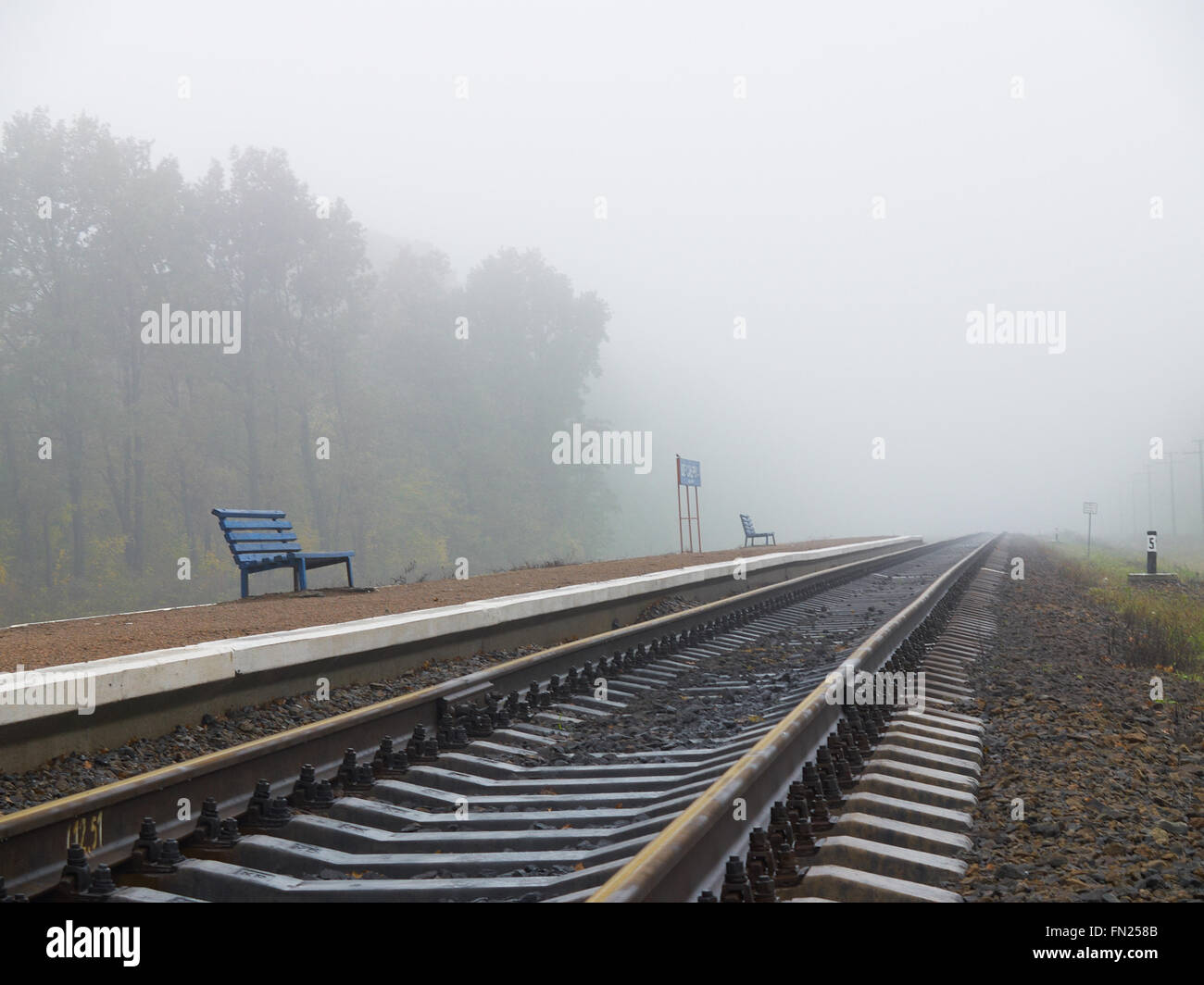 Zwei blaue Bänke auf dem Bahnsteig leer Eisenbahn an nebeligen Tag Stockfoto