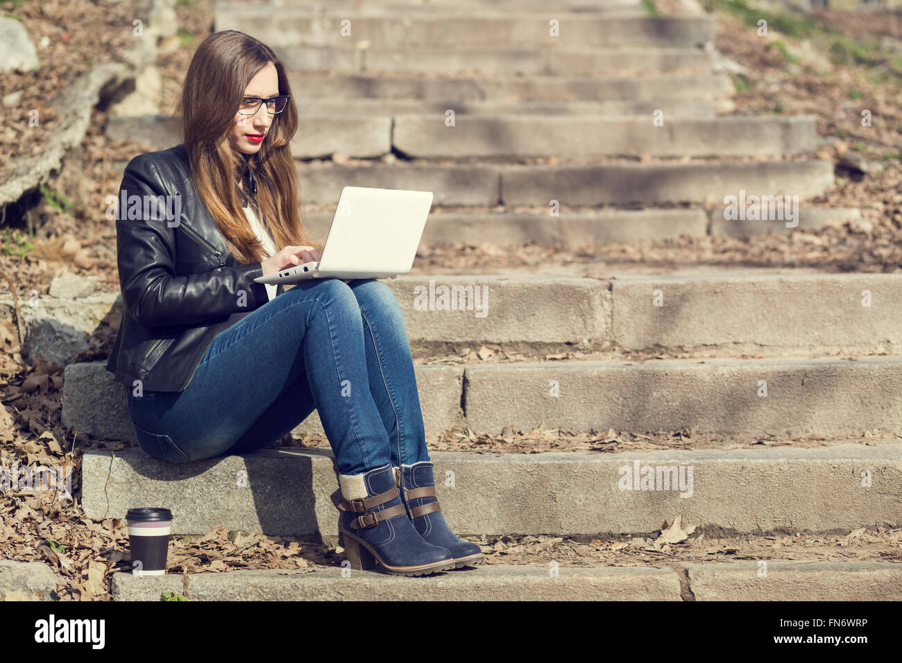 Junge Frau mit langen Haaren, die mit Laptop auf Treppe im park Stockfoto