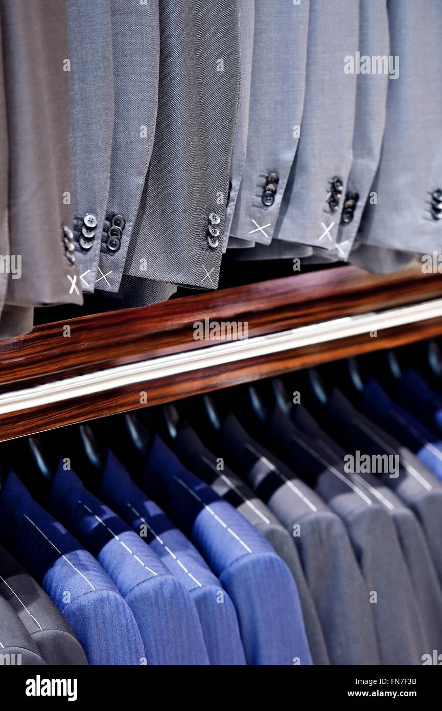 Elegante blaue und graue Anzüge auf Kleiderbügeln werden in einem Anzug-Shop gesehen. Stockfoto