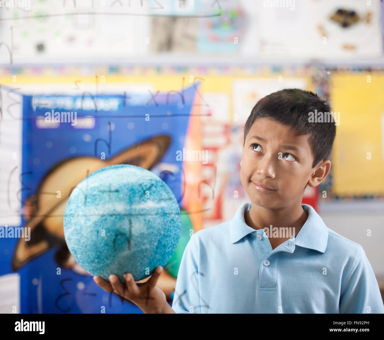 Ein Junge hält einen Globus, stehend durch eine Gleichung Board schauen verwirrt und nachdenklich. Stockfoto