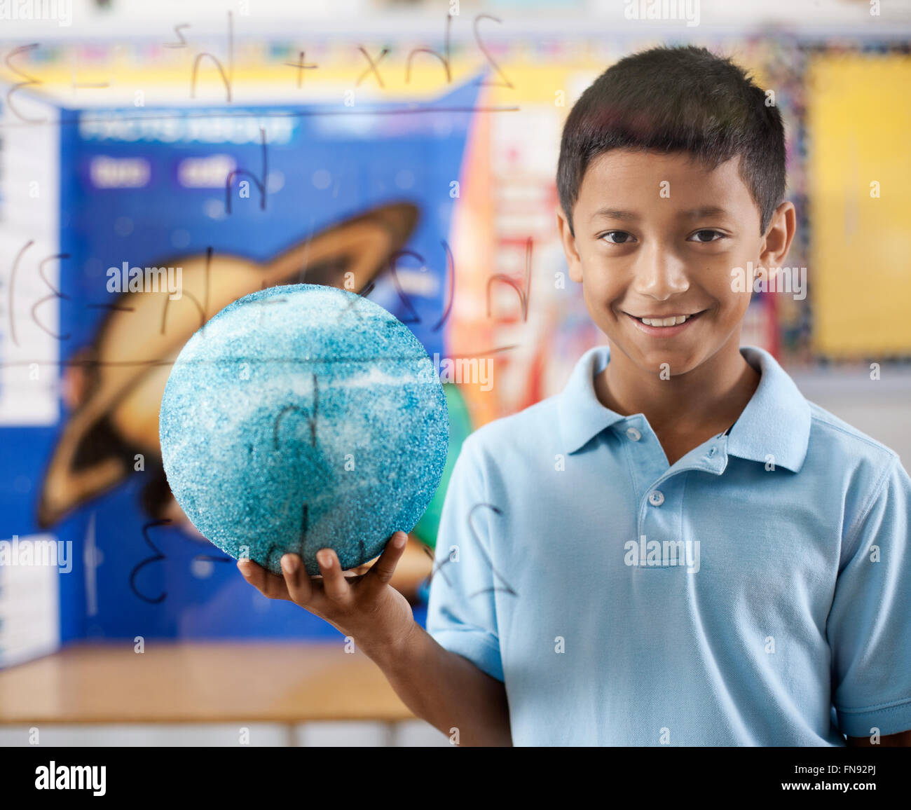 Ein Junge von einem klaren Board mit wissenschaftlichen Gleichungen stehen, hält einen Globus. Stockfoto