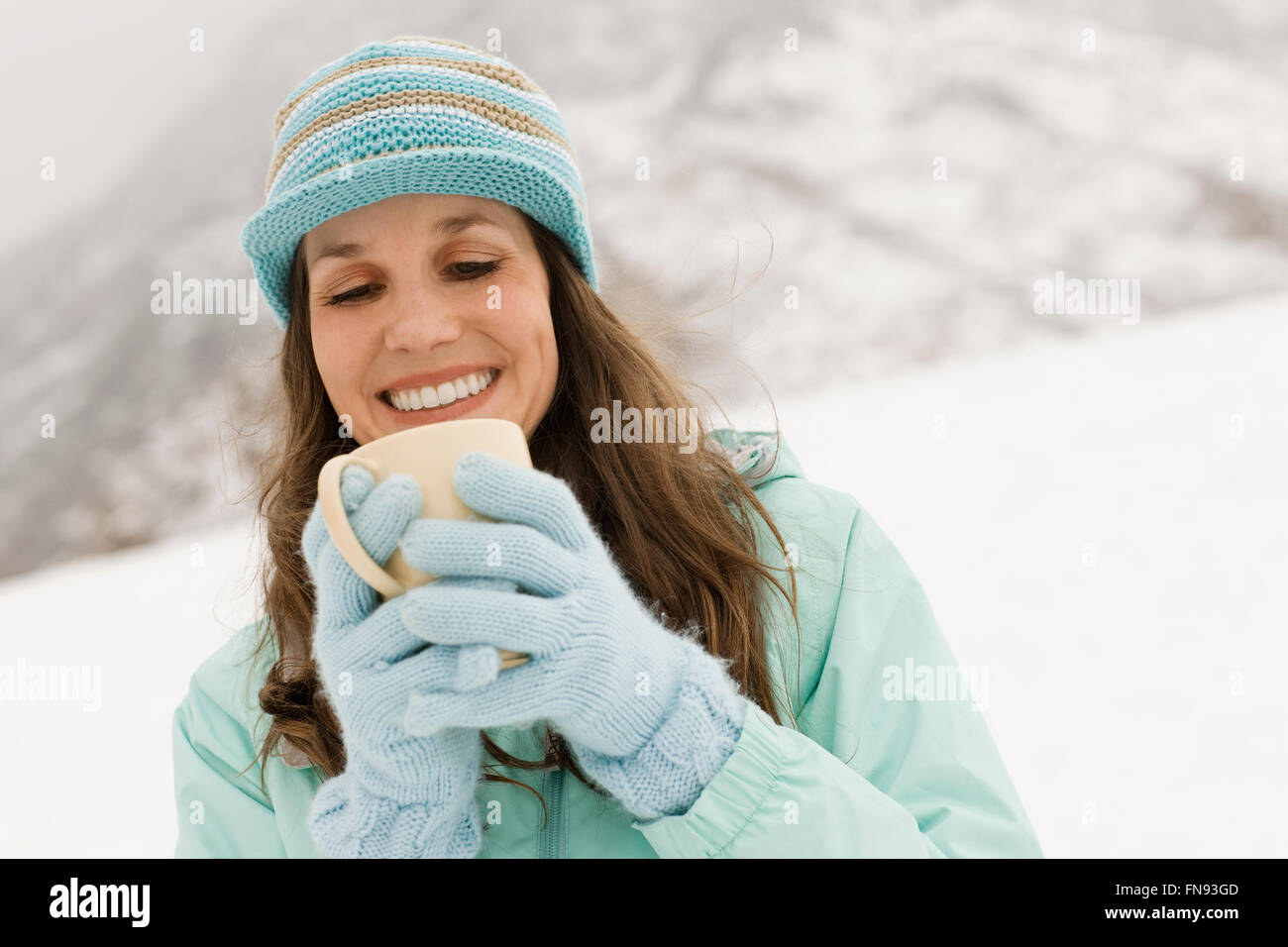 Eine Frau in einer blauen Mütze mit Handschuhen, mit einer Tasse Kaffee. Stockfoto