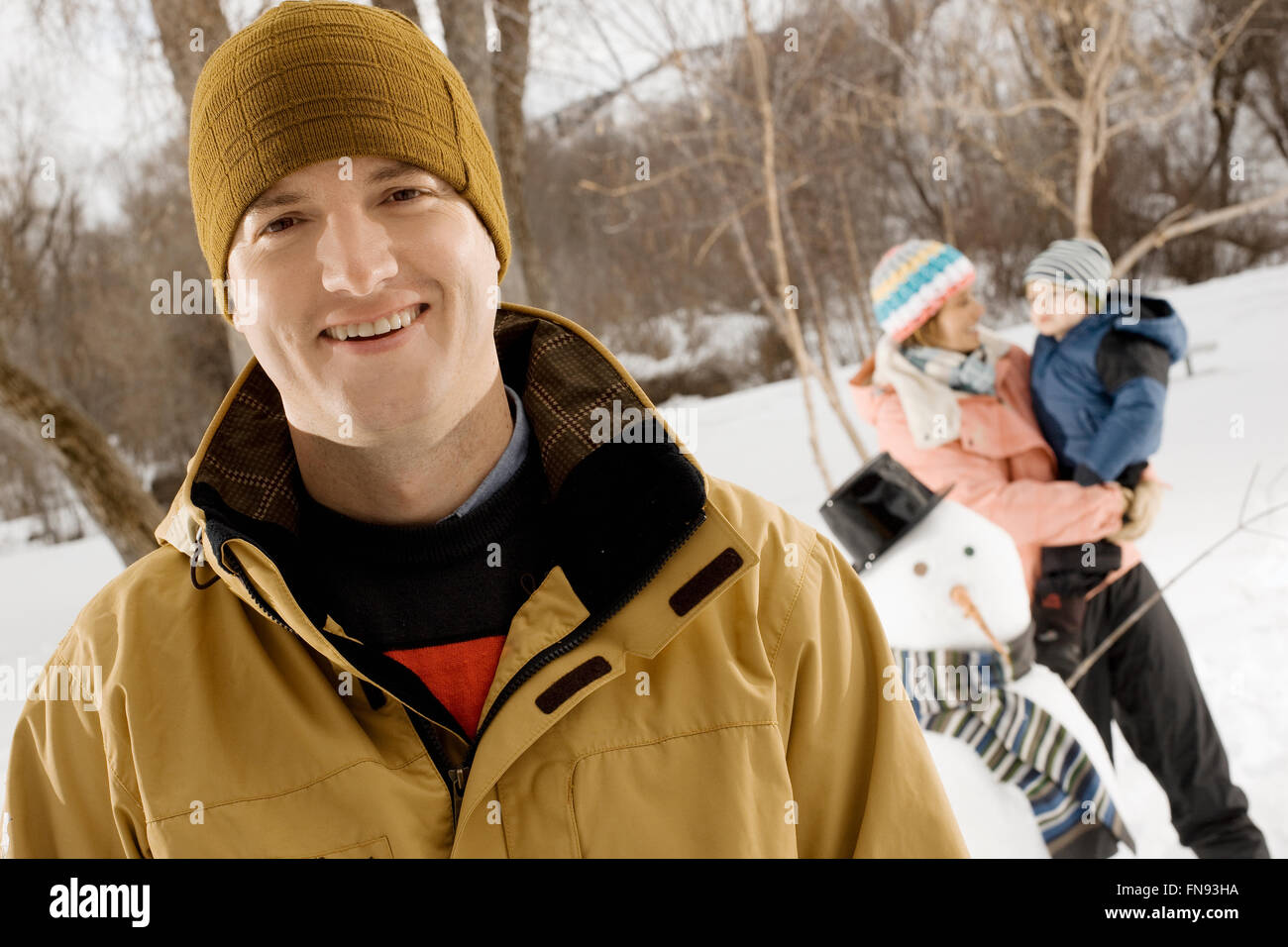 Ein Mann im Vordergrund, und eine Frau mit einem Kind neben einem Schneemann lächelnd. Stockfoto