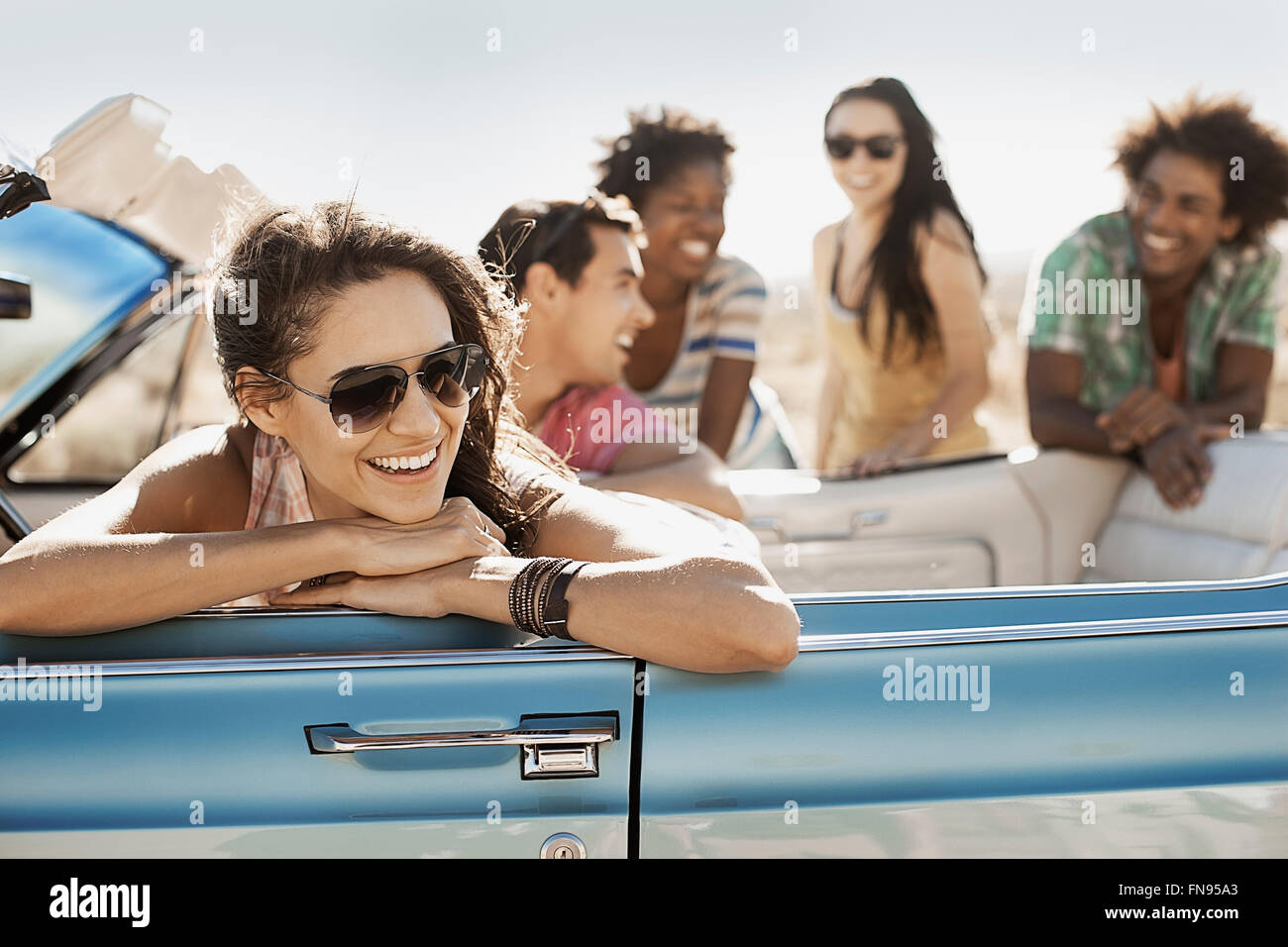 Eine Gruppe von Freunden in einem blassen Blau Cabrio auf offener Straße, fahren durch eine trockene flache Ebene, umgeben von Bergen. Stockfoto