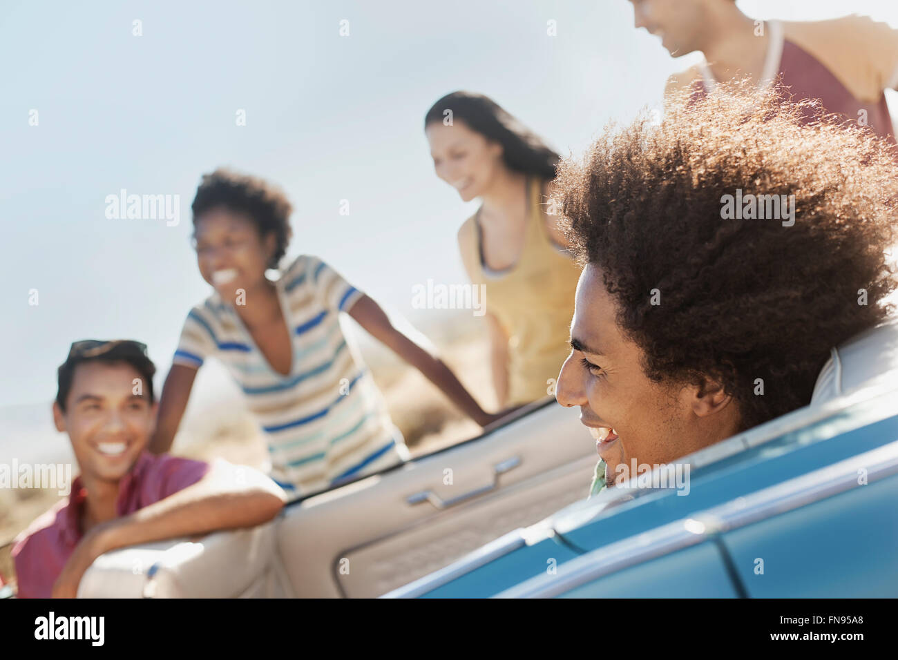 Eine Gruppe von Freunden in einem blassen Blau Cabrio auf offener Straße, fahren durch eine trockene flache Ebene, umgeben von Bergen. Stockfoto