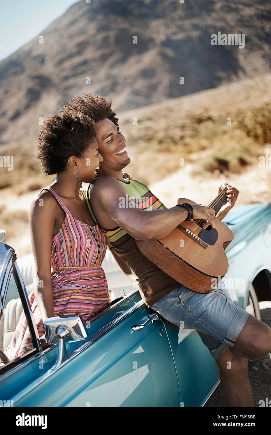 Ein junges Paar stand ein blasses blau Cabrio auf offener Straße, den Mann, eine Gitarre zu spielen. Stockfoto