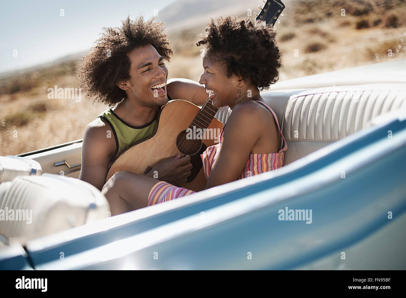 Ein junges Paar, Mann und Frau auf dem Rücksitz eines blassen blauen Cabrio Stockfoto