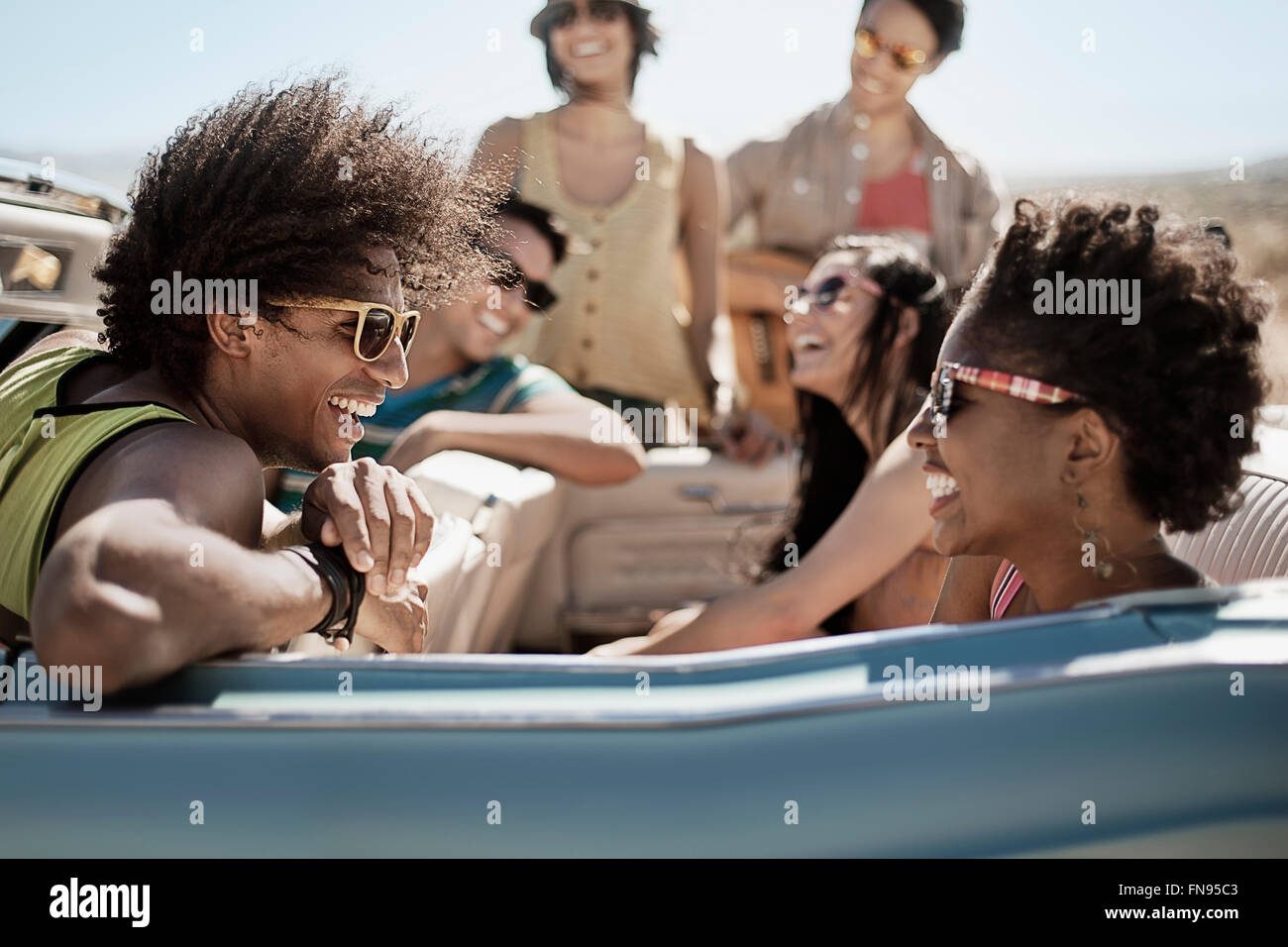 Eine Gruppe von Freunden in einem blassen Blau Cabrio auf offener Straße, fahren durch eine trockene flache Ebene, umgeben von Bergen. Stockfoto