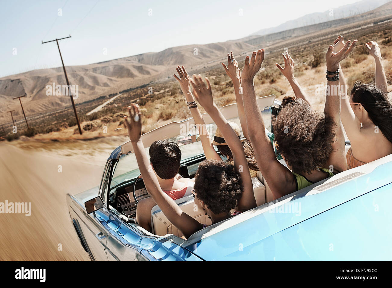 Eine Gruppe von Freunden in einem blassen Blau Cabrio auf offener Straße, fahren durch eine trockene flache Ebene, umgeben von Bergen. Stockfoto