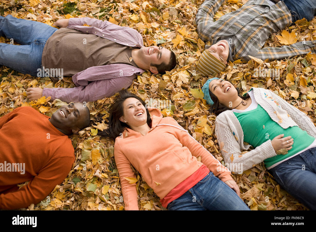 Eine Gruppe von Männern und Frauen liegen auf dem Rücken unter dem Herbstlaub. Stockfoto