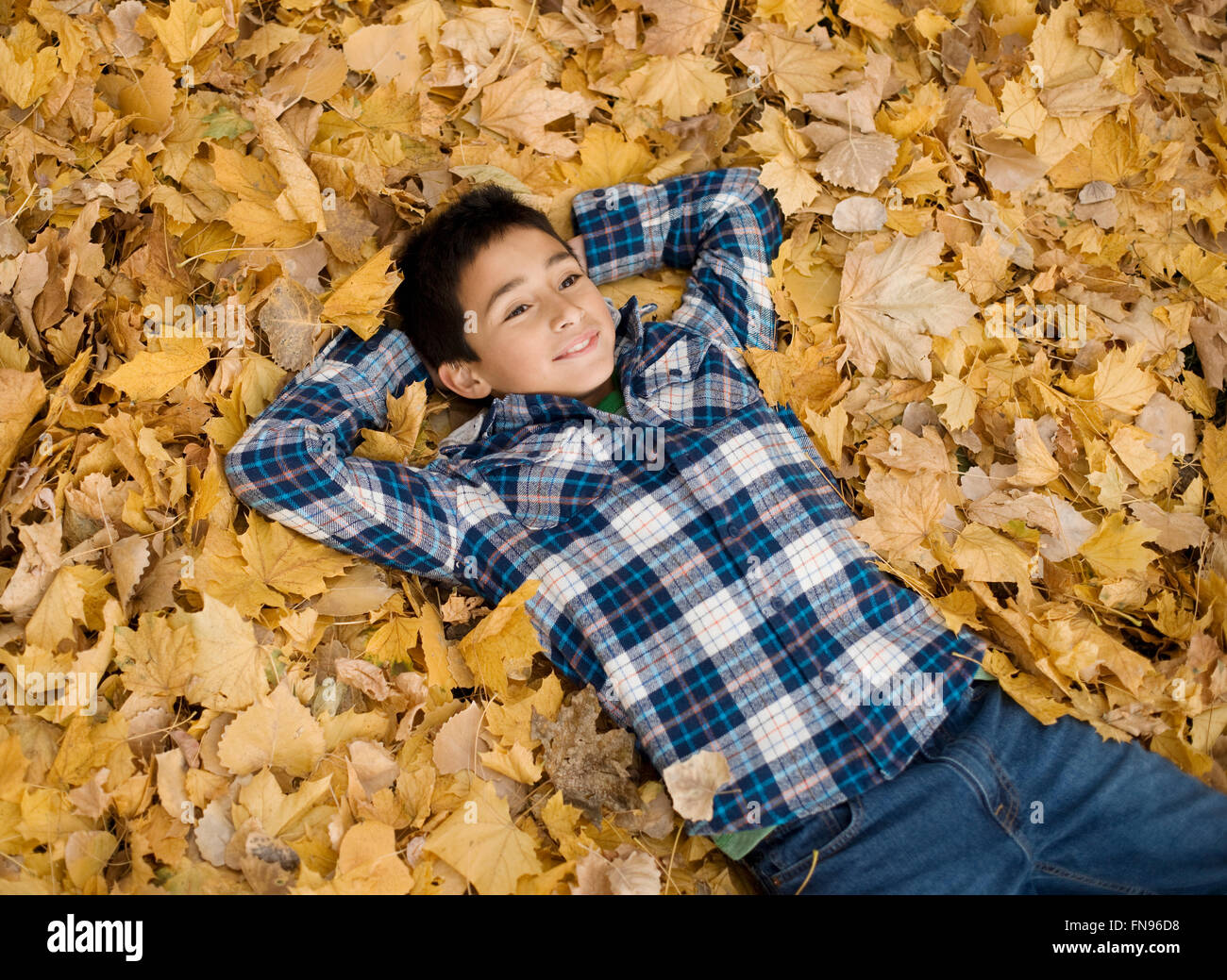 Ein Teenager in ein kariertes Hemd mit seinen Armen hinter dem Kopf auf einem Haufen Herbstlaub liegend. Stockfoto
