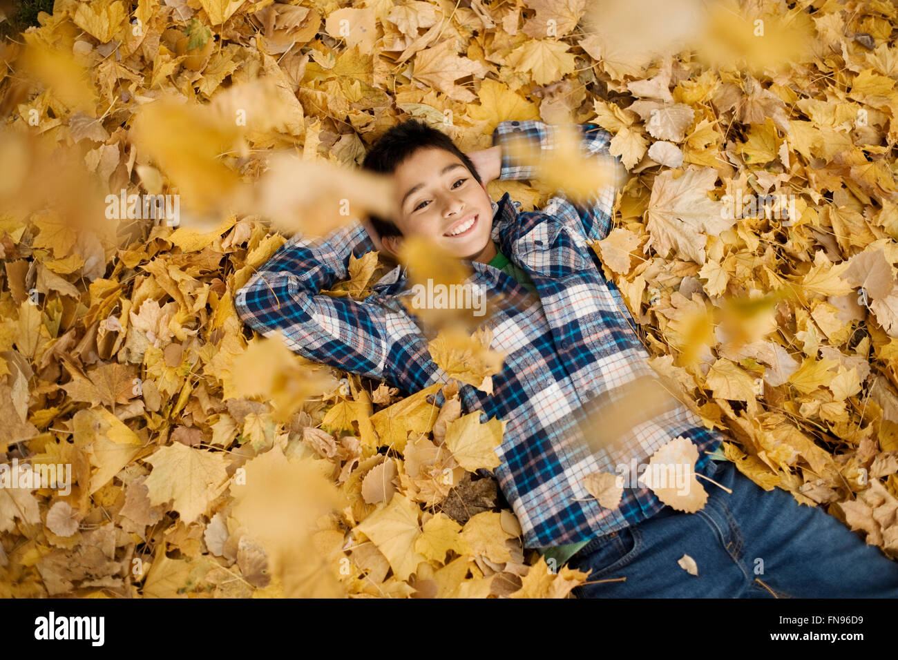 Ein Teenager in ein kariertes Hemd mit seinen Armen hinter dem Kopf auf einem Haufen Herbstlaub liegend. Stockfoto