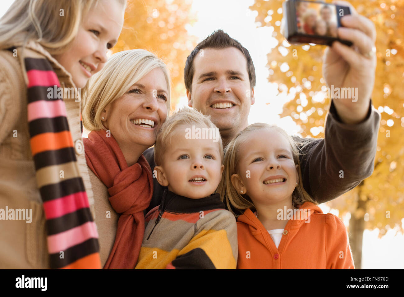 Eine Familie von beiden Eltern und seinen drei Kindern posieren für ein selfy unter das Herbstlaub an den Bäumen. Stockfoto