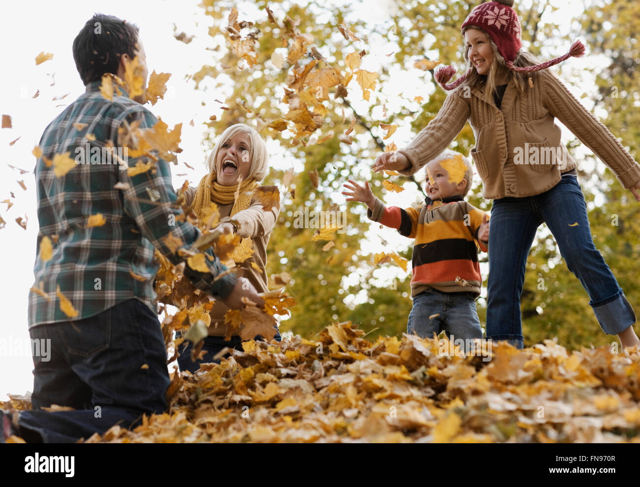 Eine Familie, Erwachsene und zwei Kinder spielen im Herbstlaub. Stockfoto