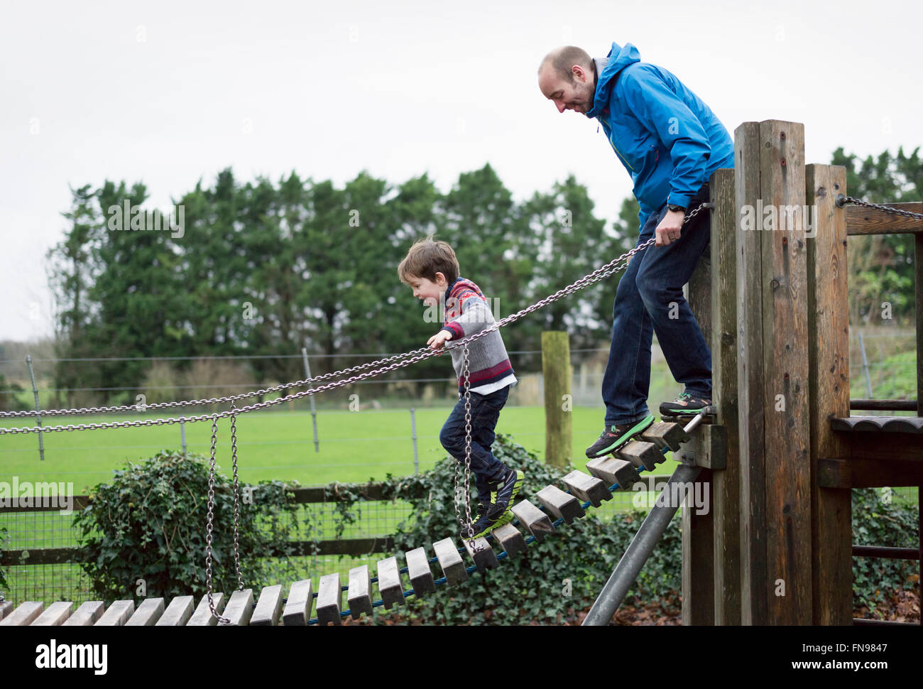 Ein Junge und sein Vater auf einem Klettergerüst, balancieren auf einem Gang. Stockfoto