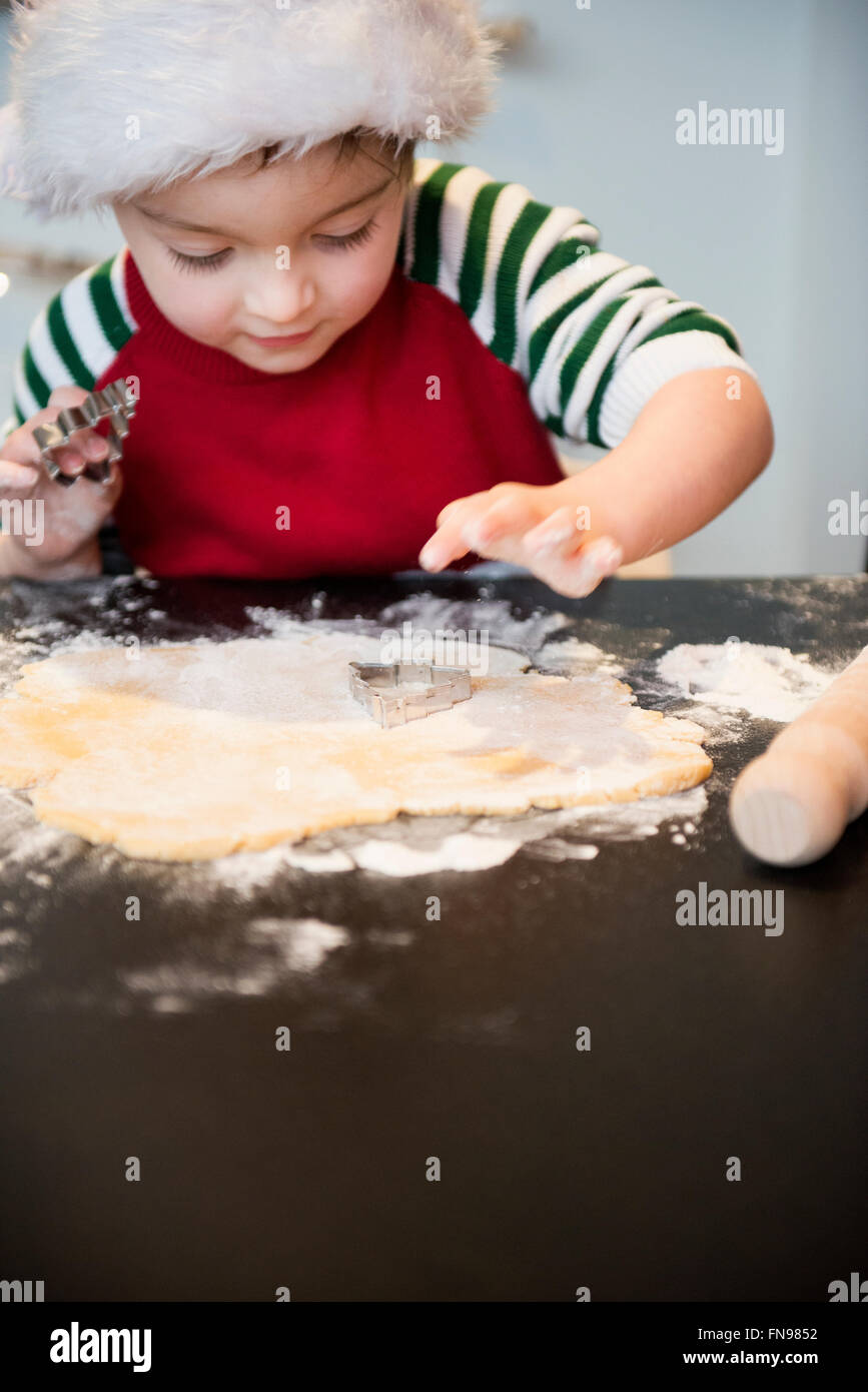 Ein Junge in eine Weihnachtsmütze Herstellung Weihnachten Kekse, Ausschneiden von Formen. Stockfoto