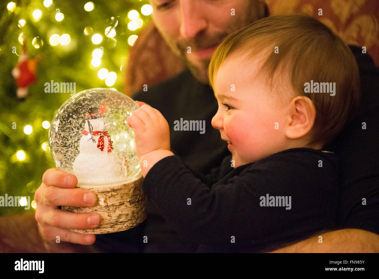 Eine Familie zu Hause am Weihnachtstag. Ein Vater und Baby Tochter betrachten eine Schneekugel. Stockfoto