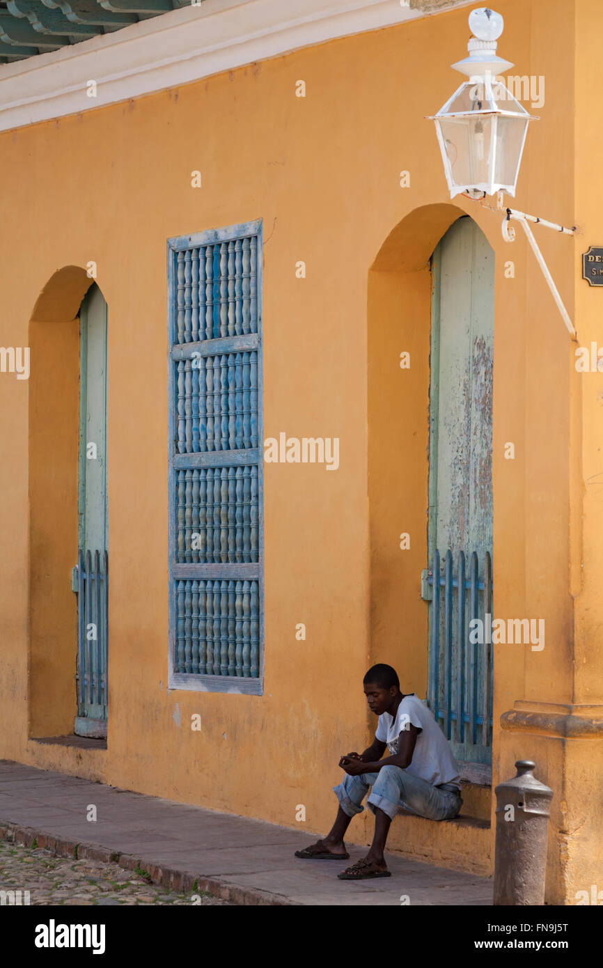Alltag in Kuba - Afro-Karibischen Mann saß vor der bunten Gebäude blickte auf Trinidad, Kuba Stockfoto