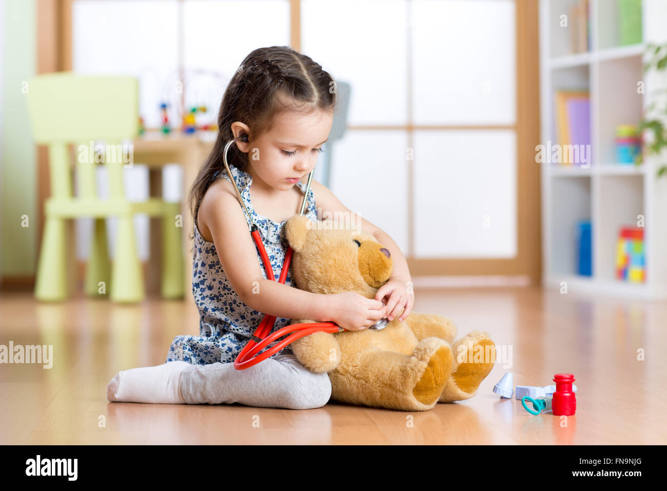 Kleines Kind Mädchen mit Stethoskop und Teddybär am Boden, auf nach Hause innen Hintergrund Stockfoto