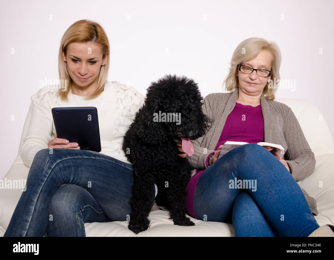 Junge Frau und ihre Mutter sitzt auf einer weißen Couch mit ihren schwarzen Pudel. Stockfoto