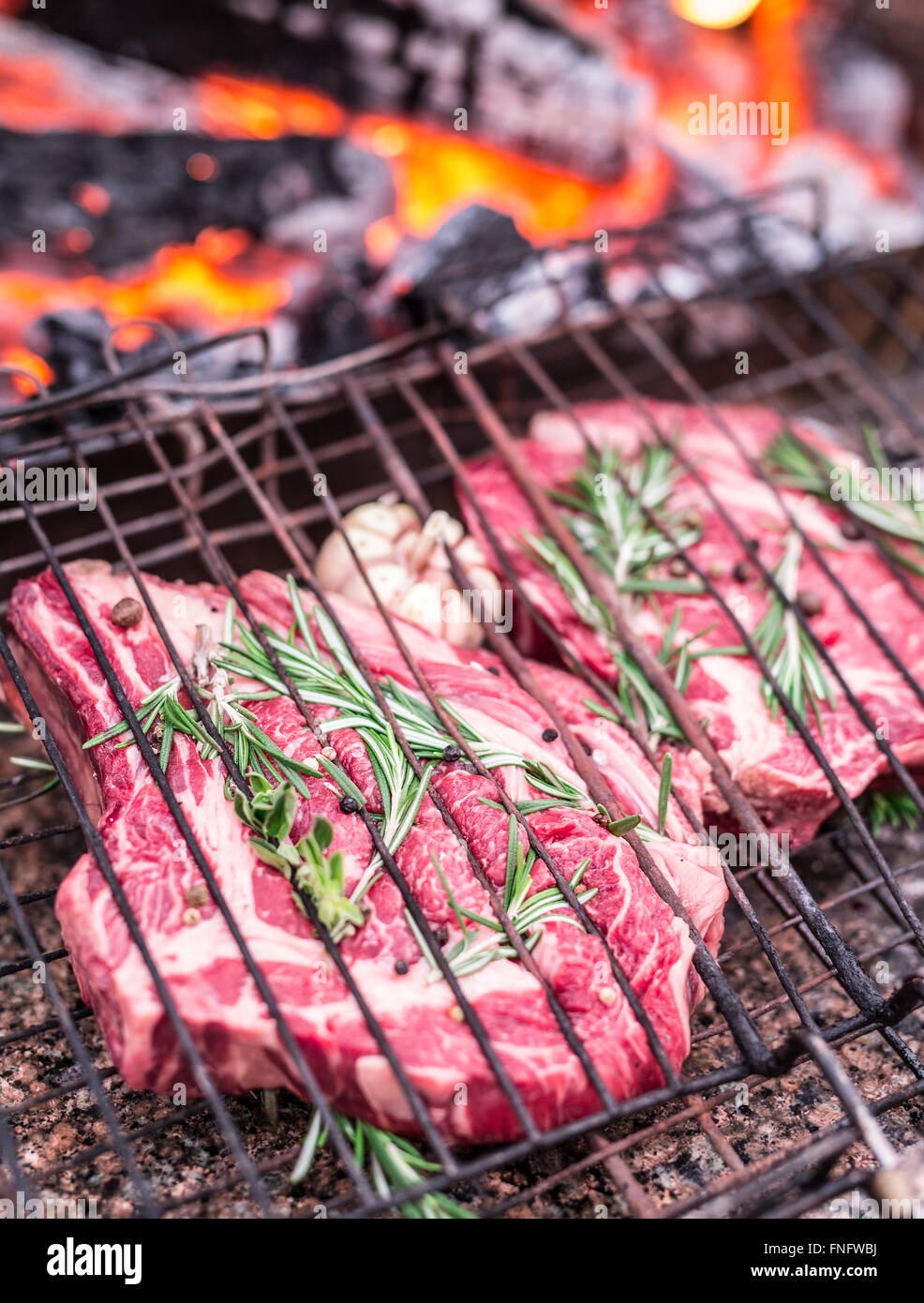 Rib-Eye-Steaks und Grill mit brennendem Feuer hinter ihnen. Stockfoto