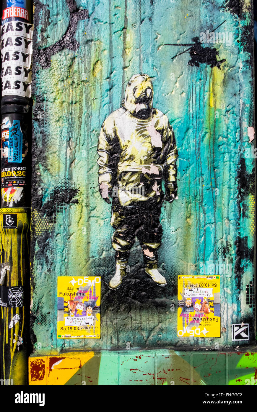 Street-Art, Graffiti. Mann, Gasmaske, schützende Stoffträgers und Hubschrauber mit atomaren Katastrophe Veranstaltungsplakate, Kreuzberg, Berlin Stockfoto