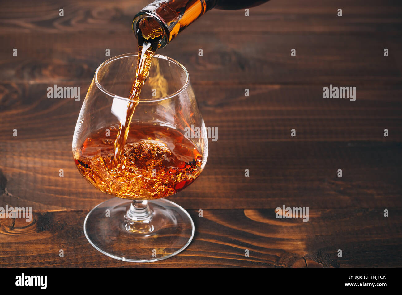 Gießen Brandy oder Cognac aus der Flasche in das Glas gegen Holz- Hintergrund Stockfoto