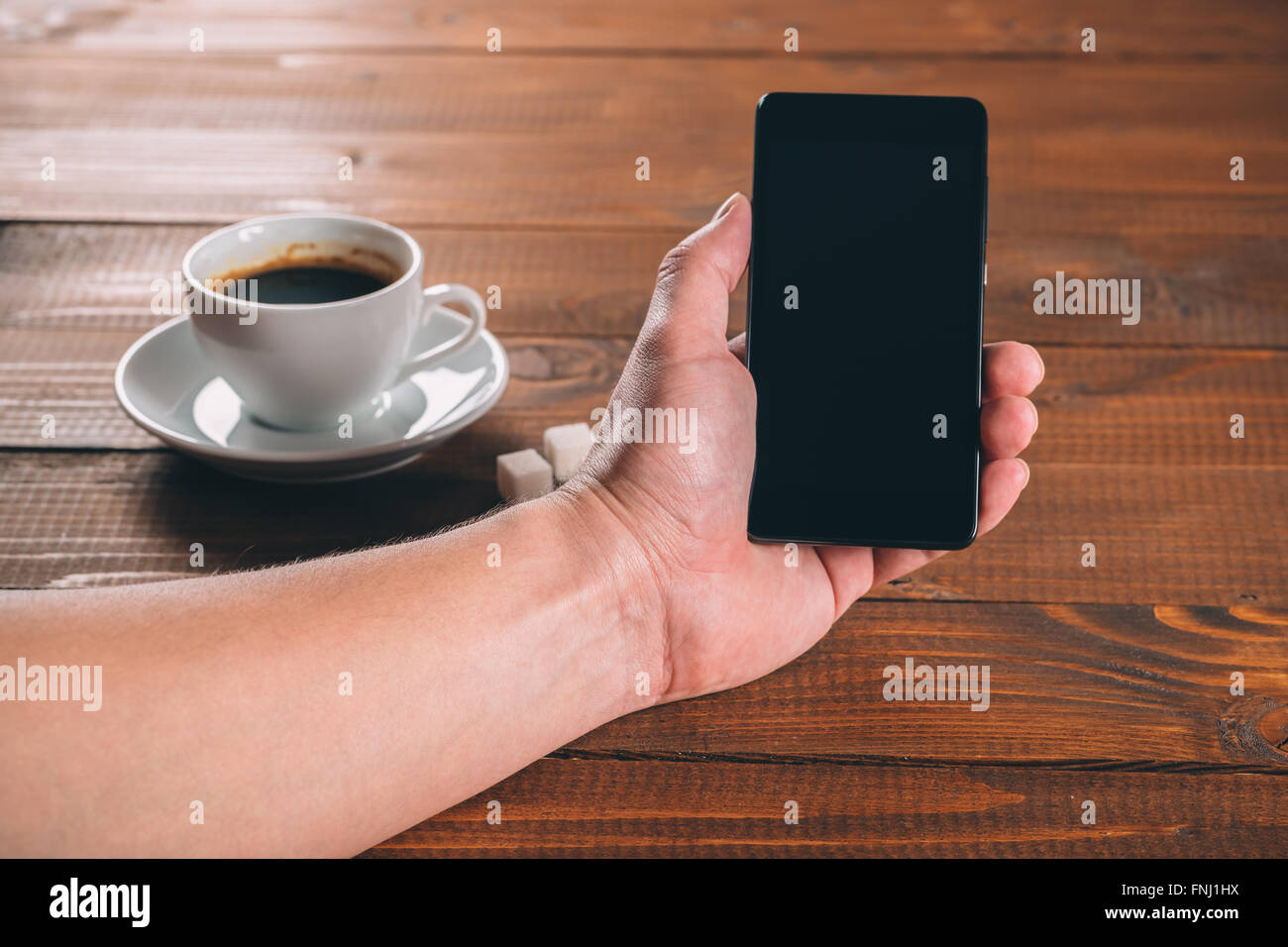 Mann Hand hält eine Telefon mit isolierten Bildschirm auf dem hölzernen Hintergrund mit Tasse Kaffee Stockfoto