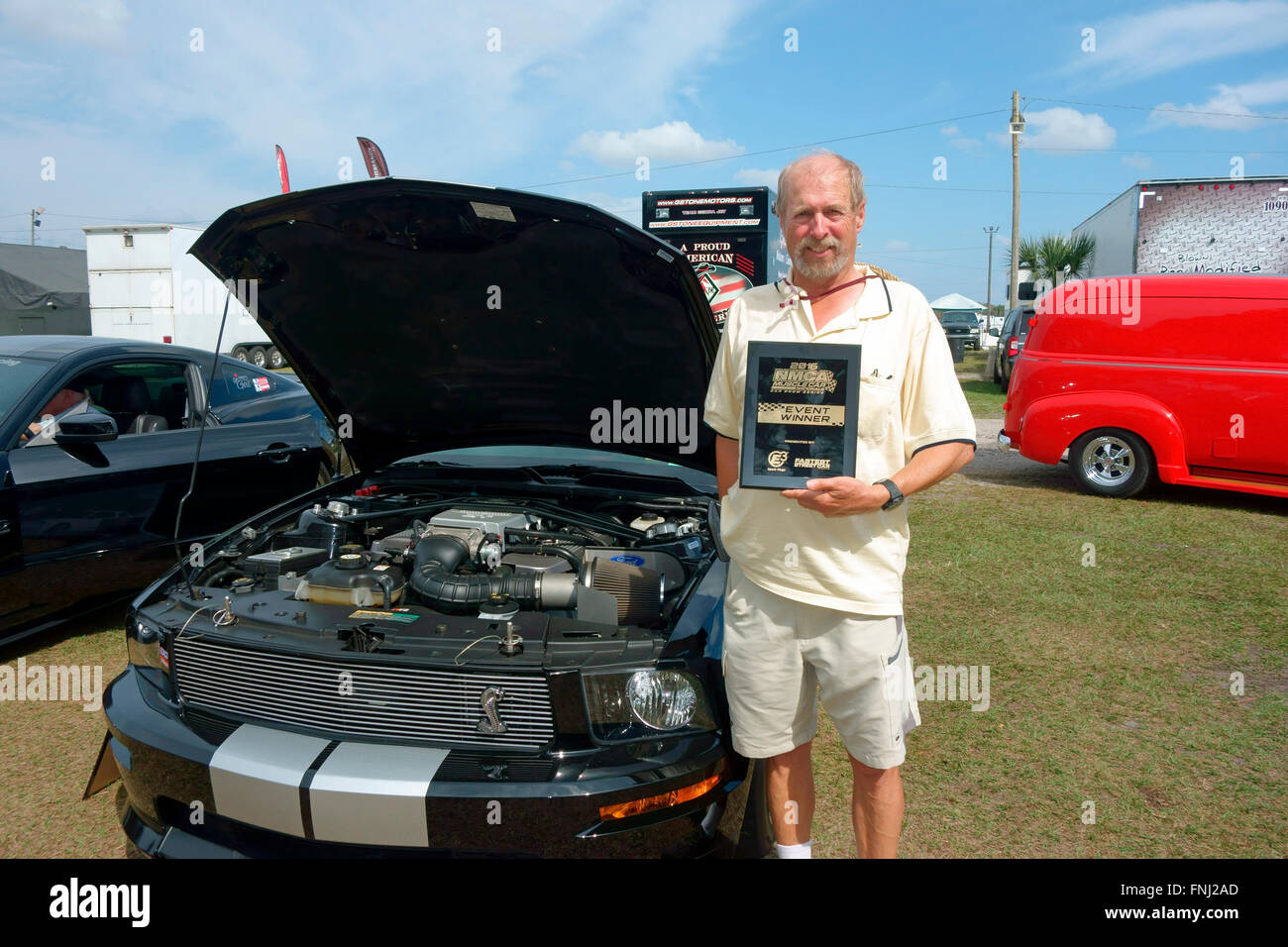 Ein Mann bei einer Autoshow, die hat den ersten Platz und hält seine Trophäe Gedenktafel neben seinem Auto Stockfoto