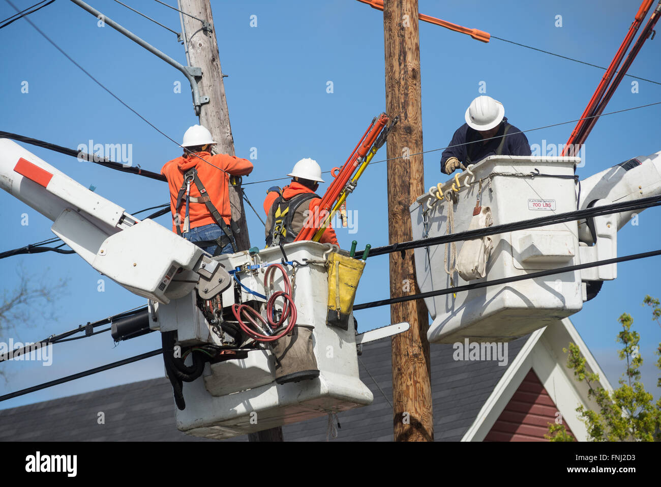 Drei Lineman in Eimern über Häuser Hign in der Luft zu schweben, wie sie arbeiten, um einen Strommast zu ersetzen. Stockfoto