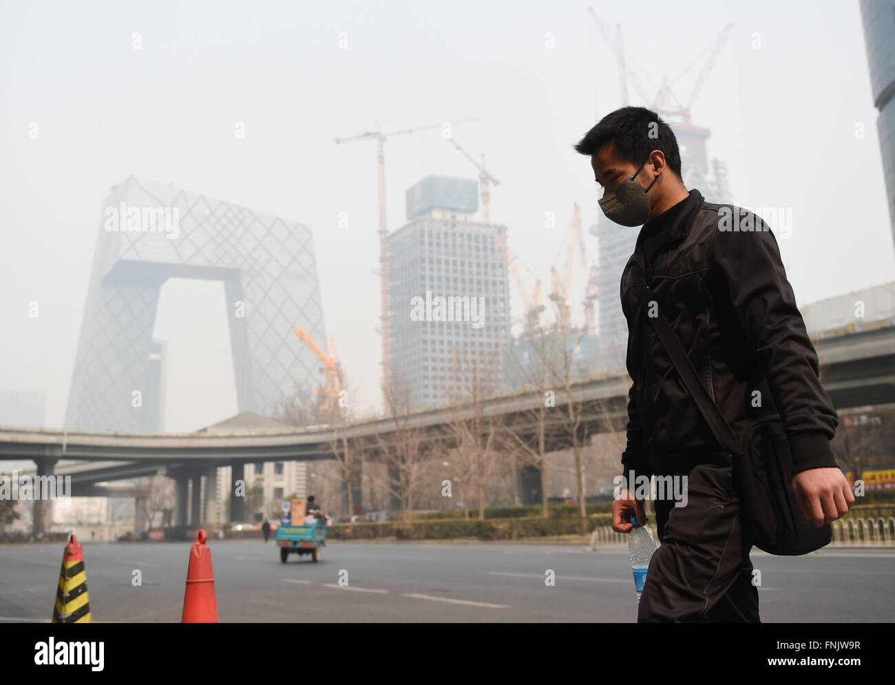 Peking, China. 16. März 2016. Ein Mann mit einer Maske geht hinter Guomao-Brücke in Peking, Hauptstadt von China, 16. März 2016. Da die Temperaturen steigen, wird die Zerstreuung der verdorbene Luft immer schwieriger. Peking und seine nahe gelegenen Tianjin und der Provinz Hebei haben Smogbound seit Anfang dieser Woche. Eine gelbe Warnung für die Luftverschmutzung ist Mittwoch Nachmittag in Peking ausgestellt. Bildnachweis: Luo Xiaoguang/Xinhua/Alamy Live-Nachrichten Stockfoto