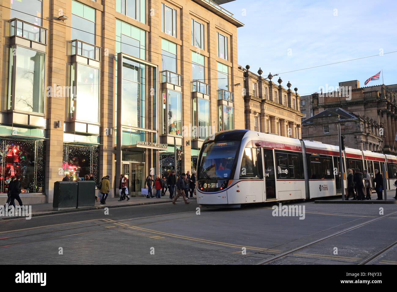 Die Edinburgh-Straßenbahn vorbei Kaufhaus Harvey Nichols, auf George Square in der Neustadt, in Schottland, Großbritannien Stockfoto