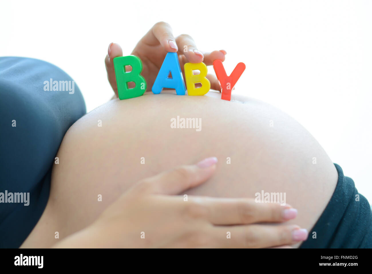 Junge werdende Mutter mit Baby auf ihren schwangeren Bauch Rechtschreibung Buchstaben-Blöcke Stockfoto