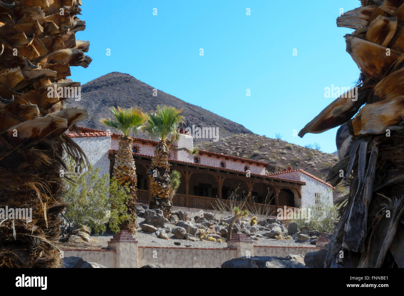 Auf der Suche zwischen zwei Bäumen auf ein weißes Gebäude mit roten Ziegeldach. Scottys Castle Death Valley. Stockfoto