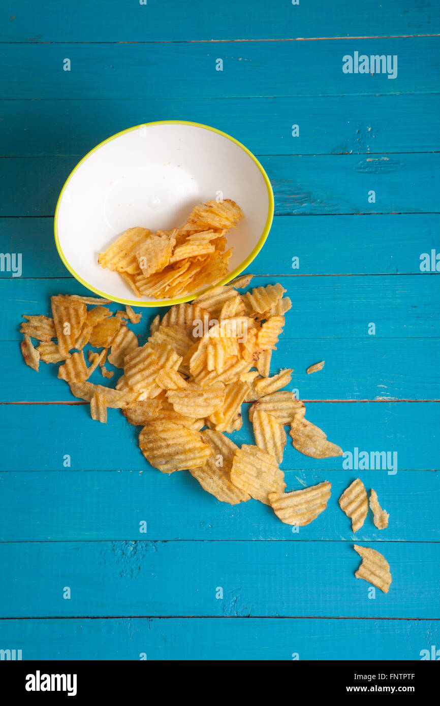 Kartoffel-Chips aus der Platte auf einem blauen Holztisch gegossen Stockfoto