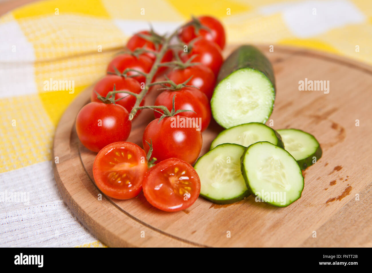 Cherry-Tomaten und Gurken in Scheiben schneiden, auf einem Holzbrett Stockfoto