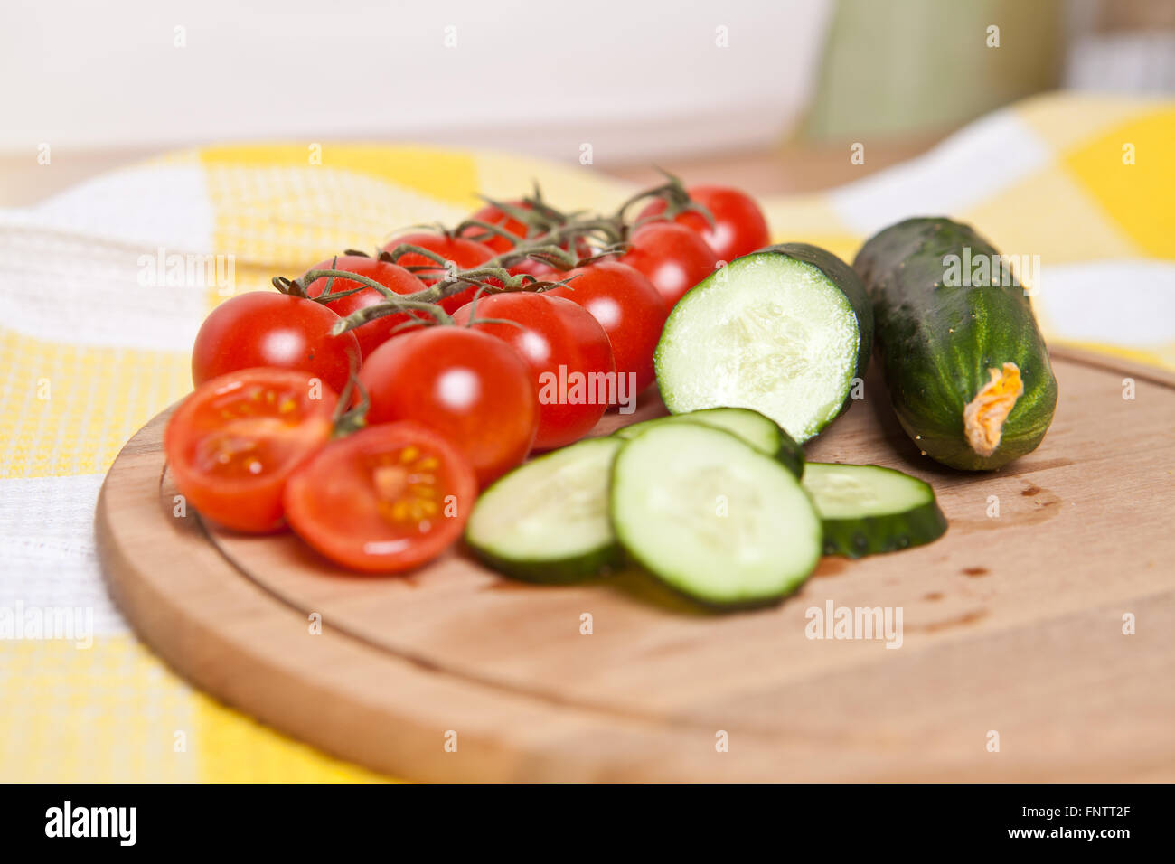 Cherry-Tomaten und Gurken in Scheiben schneiden, auf einem Holzbrett Stockfoto