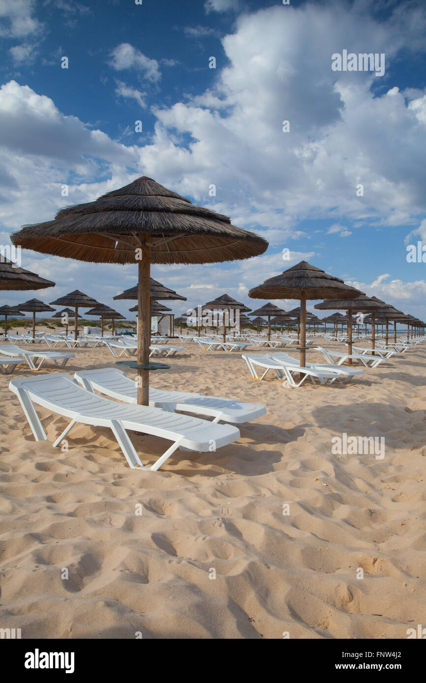 Verschiedene Sonnenschirme und Liegestühle am leeren Strand auf der Insel Tavira, Algarve. Portugal Stockfoto