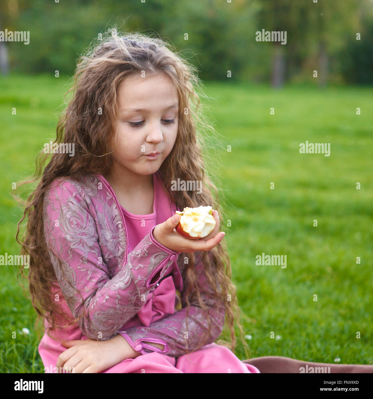 Mädchen einen Apfel essen, in einem Sommerpark sitzen auf ein kariertes Stockfoto