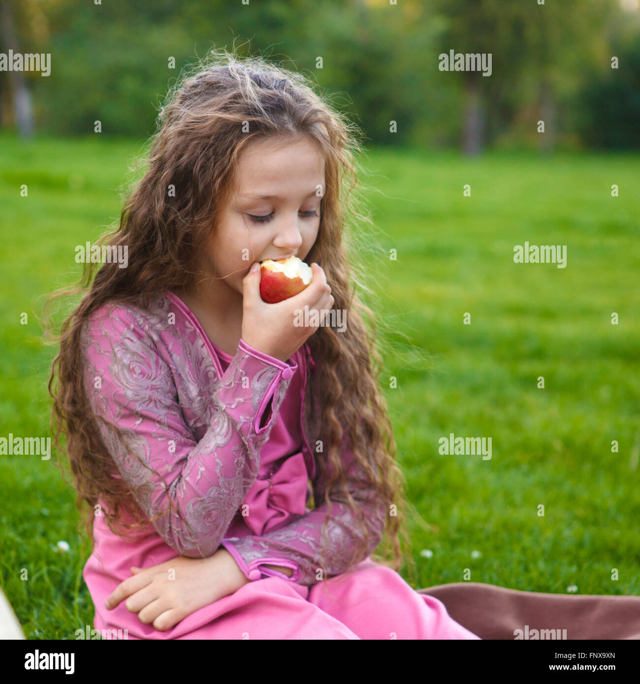 Mädchen einen Apfel essen, in einem Sommerpark sitzen auf ein kariertes Stockfoto