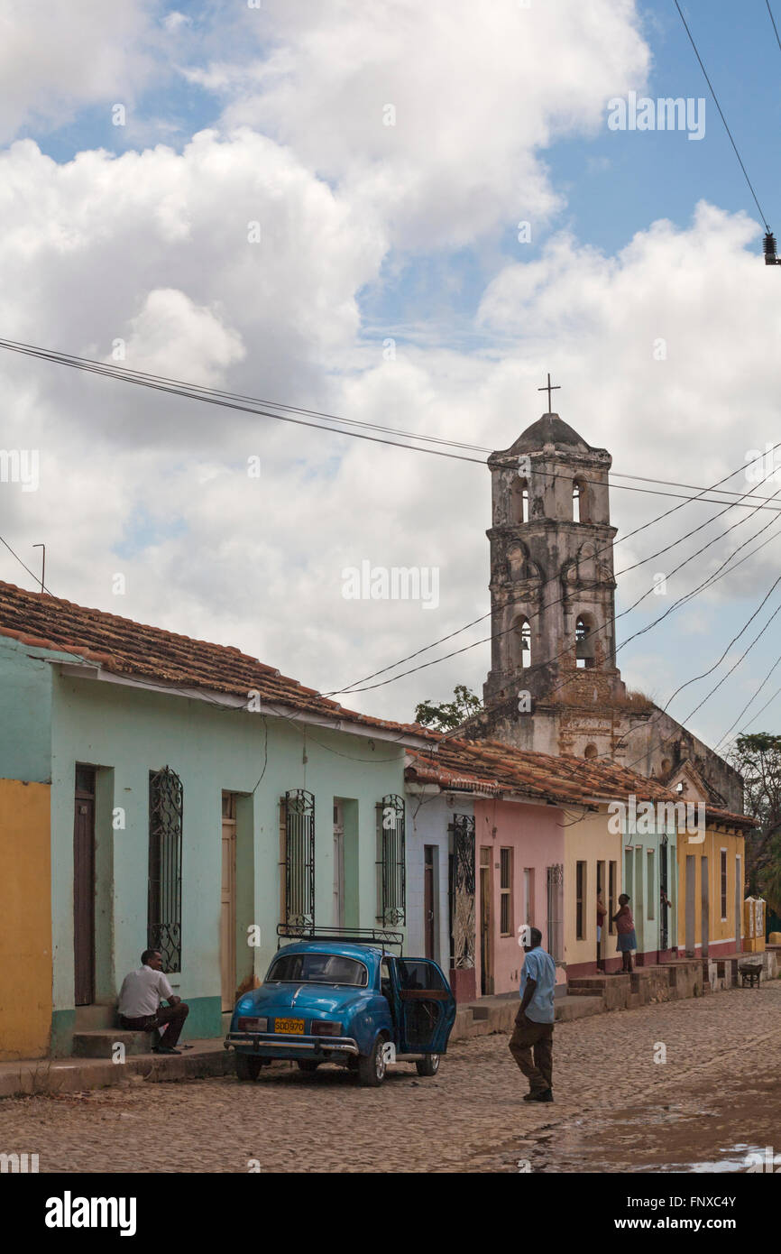 Alltag in Kuba - arbeiten am Auto in der Straße mit zerstörten Kirche Iglesia de Santa Ana in der Ferne auf Trinidad, Kuba im März Stockfoto