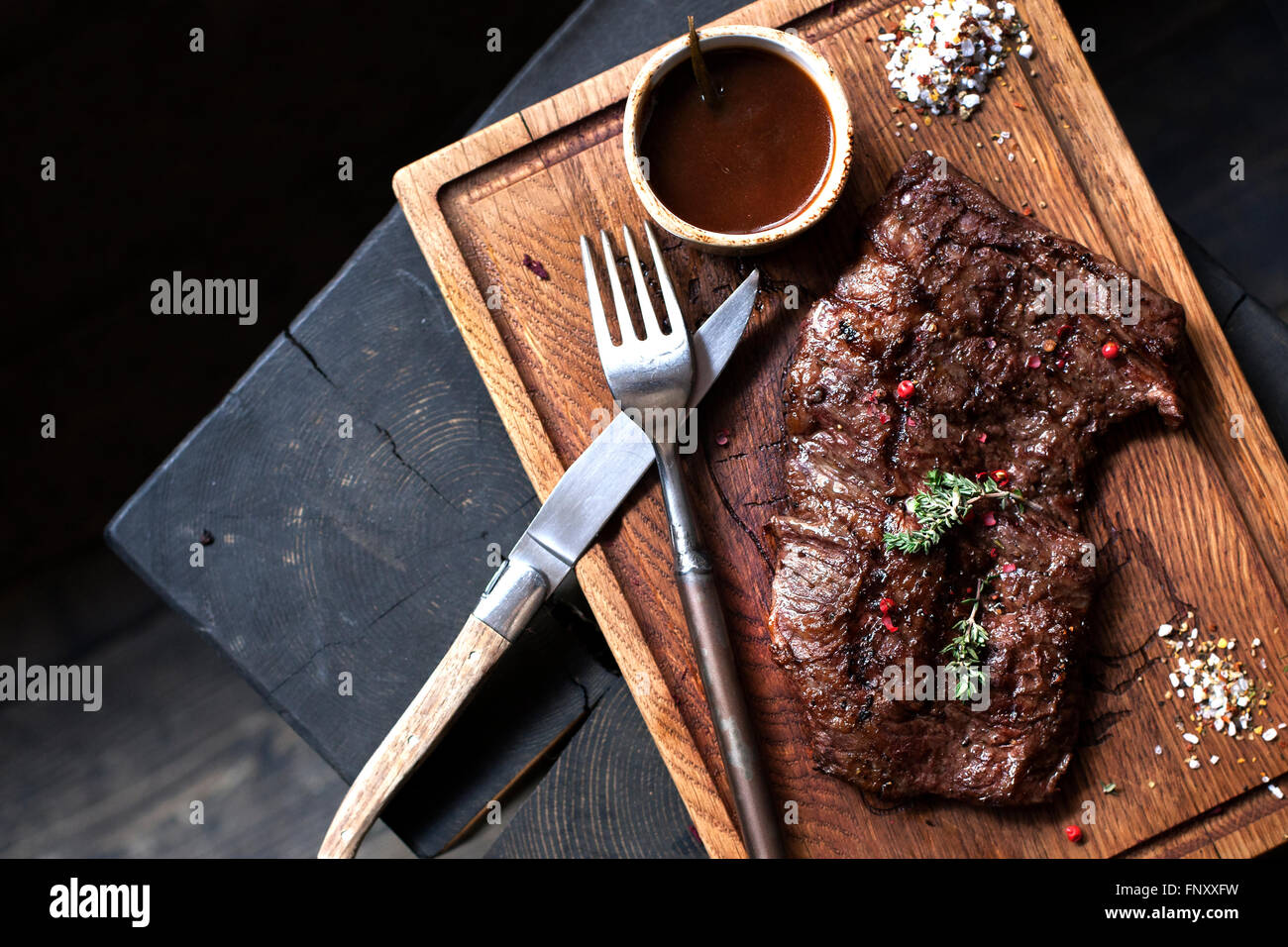 Beefsteak. Stück Rindfleisch vom Grill BBQ mariniert mit Gewürzen und Kräutern auf rustikalem Holzbrett über groben hölzernen Schreibtisch mit Textfreiraum Stockfoto