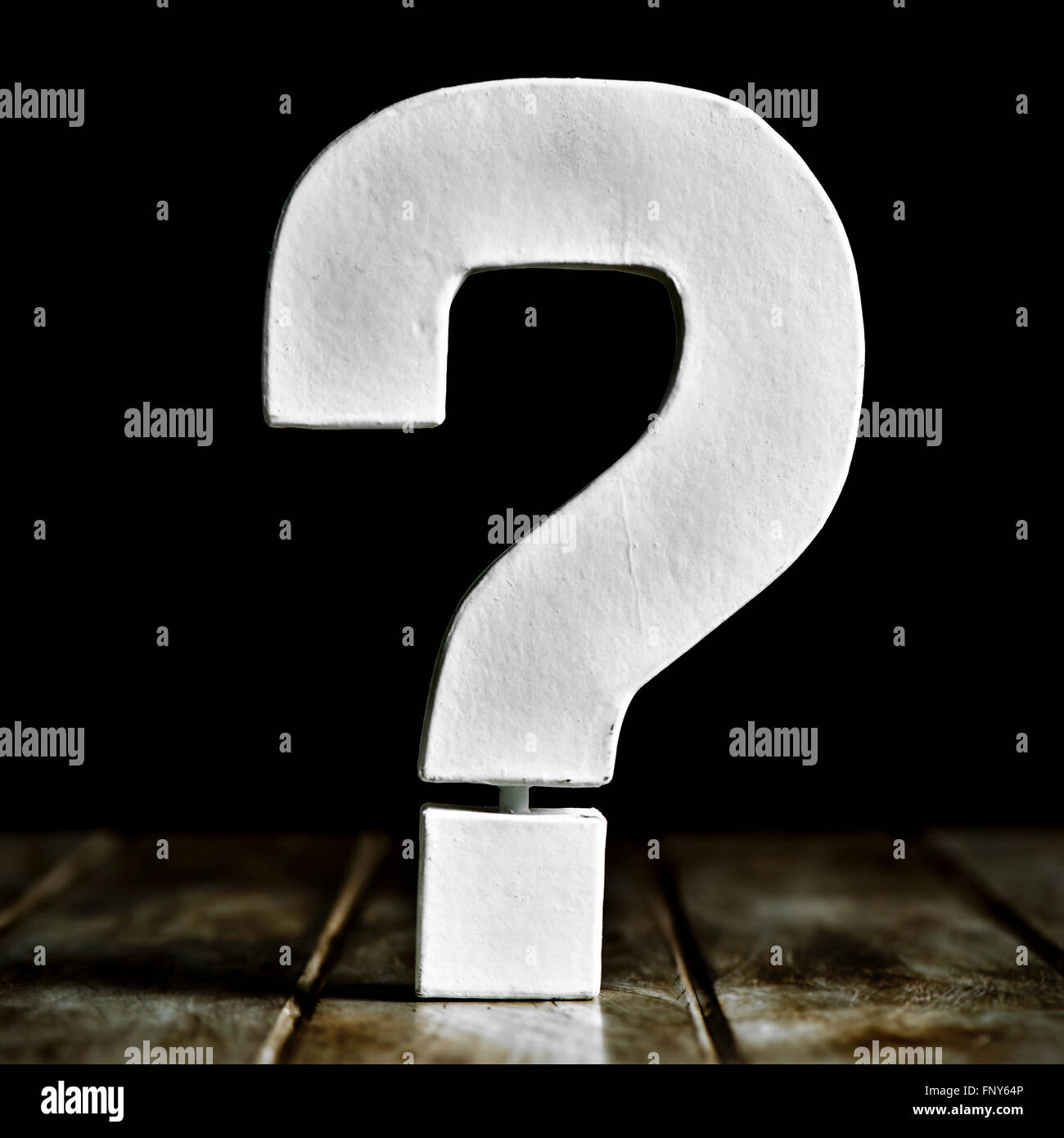 eine weiße dreidimensionale Fragezeichen auf einer rustikalen Holzoberfläche vor schwarzem Hintergrund Stockfoto