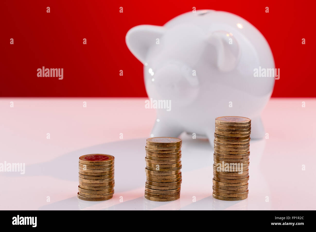 Weiße Sparschwein mit Stapel der Münzen Stockfoto